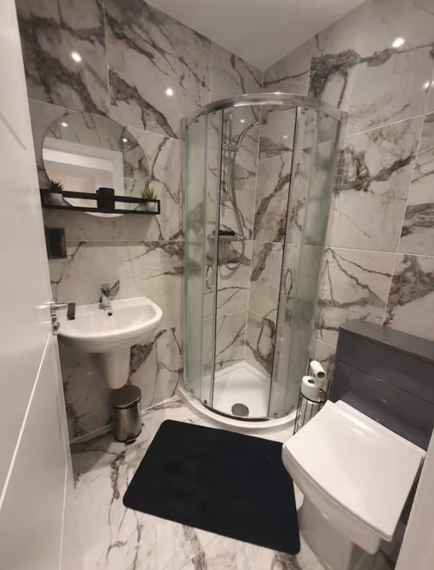 Modern bathroom with marble walls, corner shower enclosure, pedestal sink and toilet