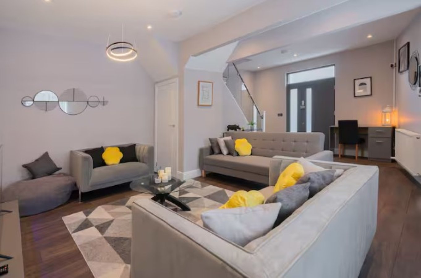 Modern open-plan living room with gray sofas, yellow cushions, geometric rug and staircase