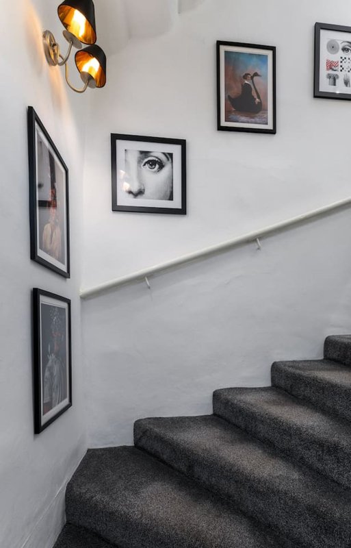 Staircase with dark carpet, white walls, framed black-and-white photographs, and brass wall sconces