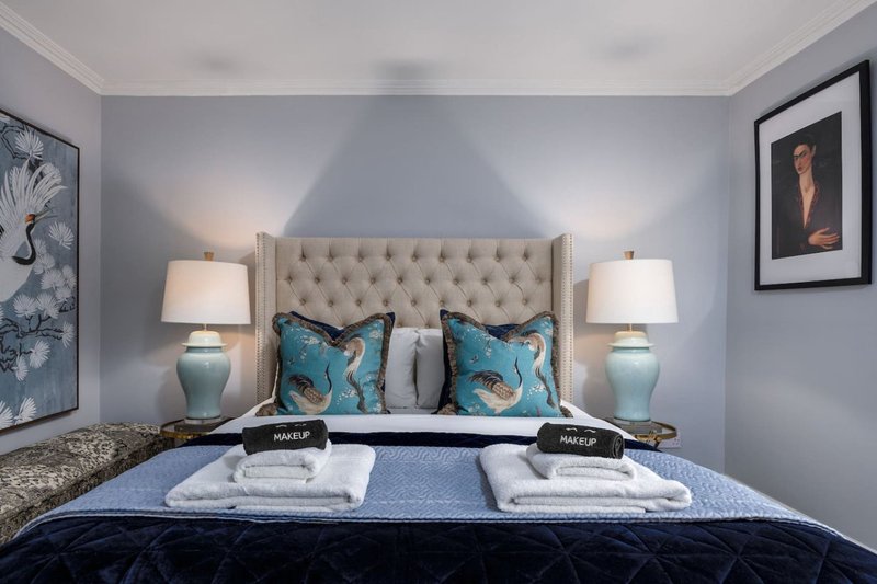 Modern bedroom with upholstered headboard, turquoise patterned pillows, bedside lamps and framed wall art
