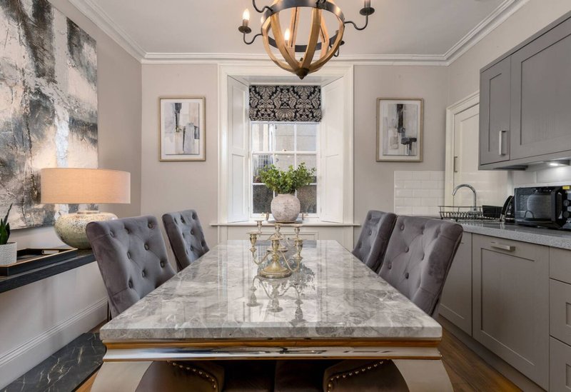 Open-plan kitchen and dining area with marble table, grey upholstered chairs, and modern cabinetry