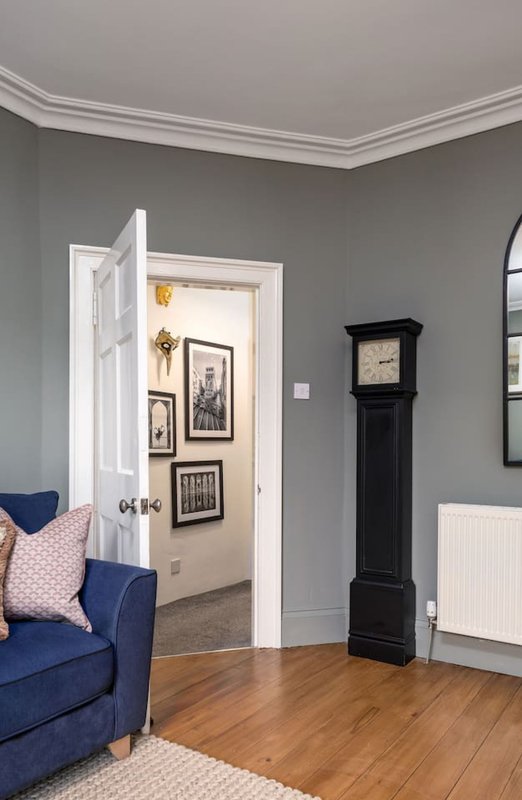 Living room with blue sofa, wooden floor, gray walls, open doorway and black grandfather clock