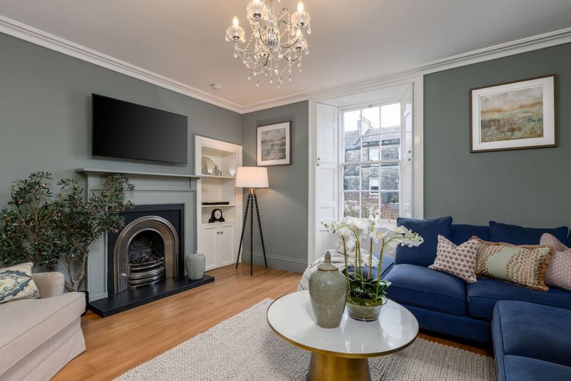 Living room with fireplace, blue sofa, wooden floor, and large windows