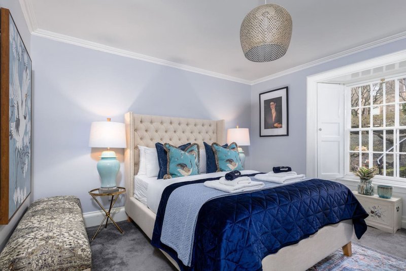 Bright bedroom with upholstered headboard, blue bedding, pendant lamp, and large windows
