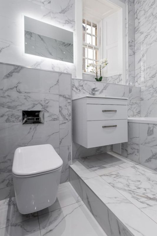 Modern bathroom with marble tiles, wall-mounted vanity, illuminated mirror and toilet