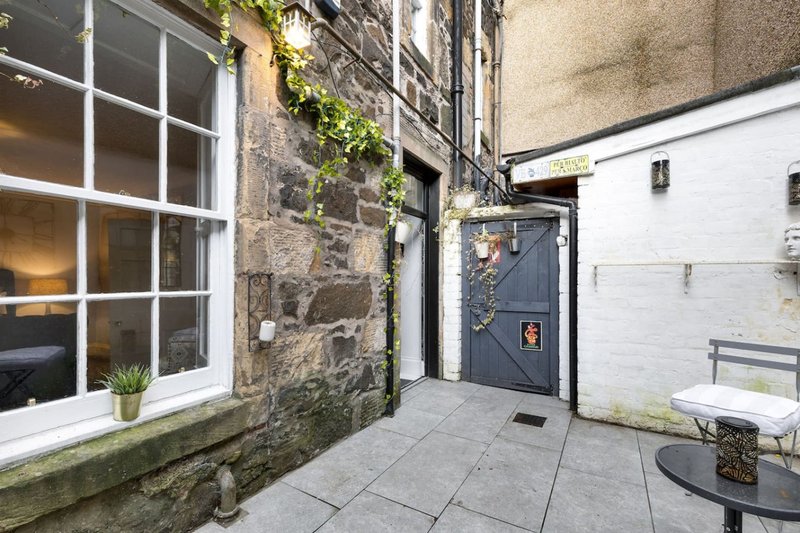 Exterior courtyard with stone building, dark wooden door, white garage, and paved seating area