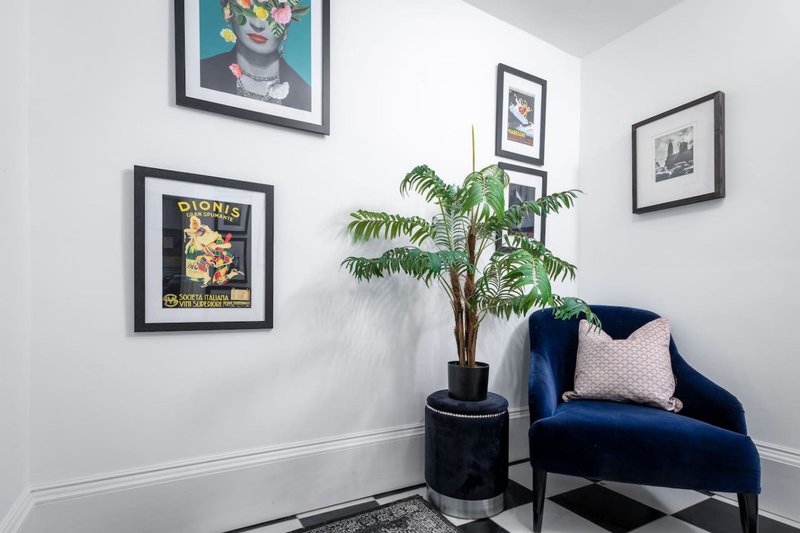 Modern living room corner with blue velvet armchair, potted plant, and framed wall art