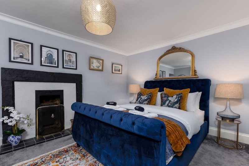 Bedroom with blue velvet bed, fireplace, gold mirror, framed wall art and pendant light