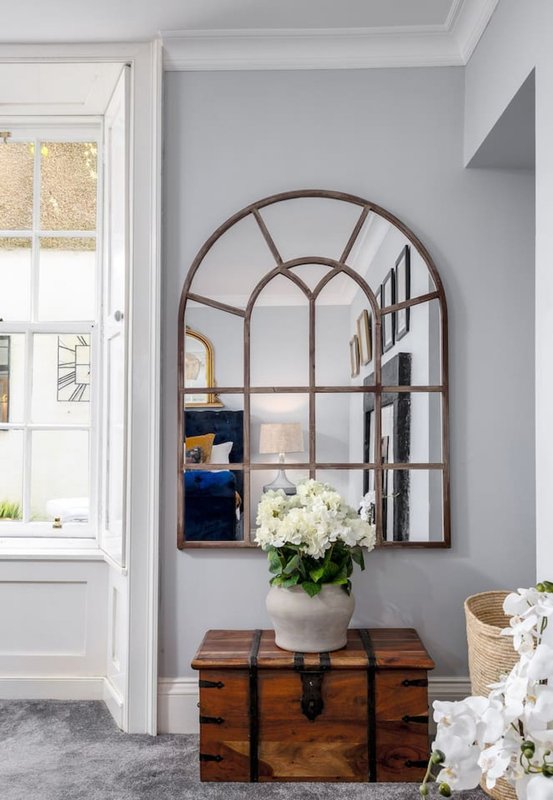 Entryway with arched mirror, wooden trunk, white flowers in vase, and door to garden