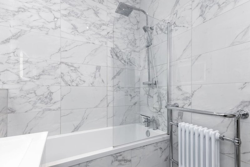 Modern bathroom with marble-effect tiles, white bathtub, glass shower screen and heated towel rail
