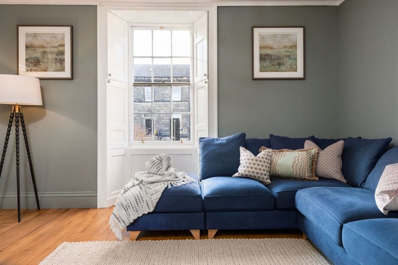 Bright living room with blue sofa, wooden floor, framed artwork and tall window