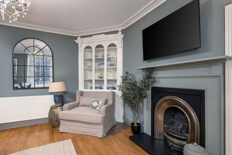 Modern living room with fireplace, grey walls, armchair, TV, and decorative mirror