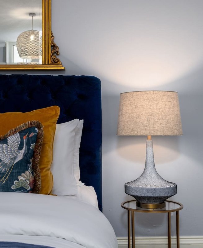 Modern bedroom with navy upholstered headboard, gold and blue decorative pillow, bedside lamp and gold-framed mirror