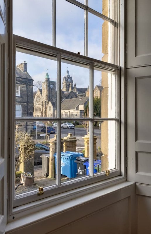 Window view of historic stone buildings and street with blue bins below