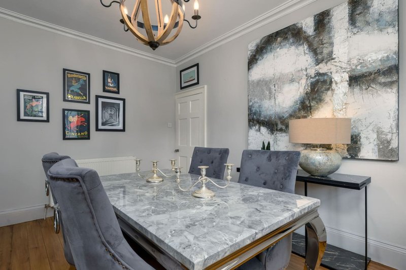 Dining room with marble table, grey upholstered chairs, artwork on walls, and pendant lighting