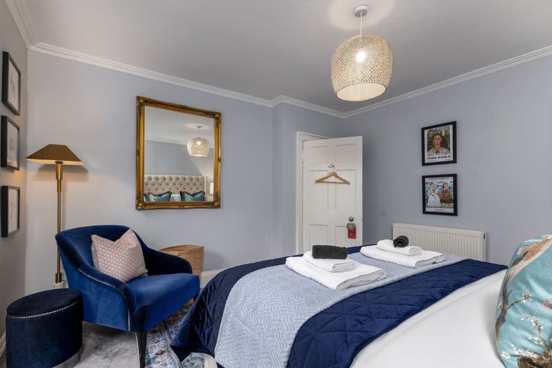 Bedroom with double bed, blue velvet armchair, pendant light and framed wall art