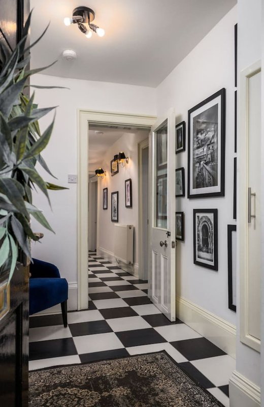 Modern hallway with black and white checkered floor, framed wall art, and potted plant