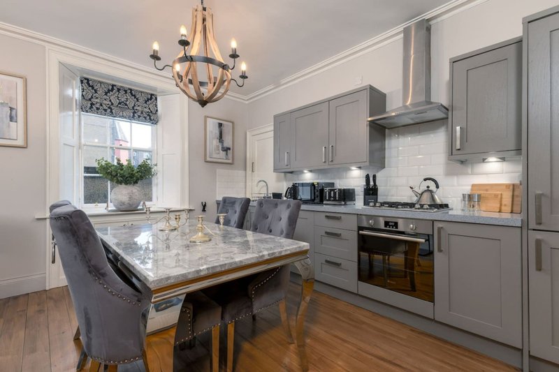 Modern kitchen with gray cabinetry, marble island, dining chairs, and pendant lighting