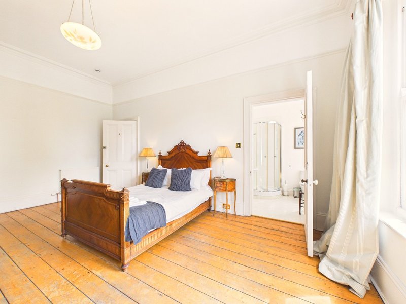 Bright bedroom with wooden bed frame, blue bedding, wooden floor and pendant light
