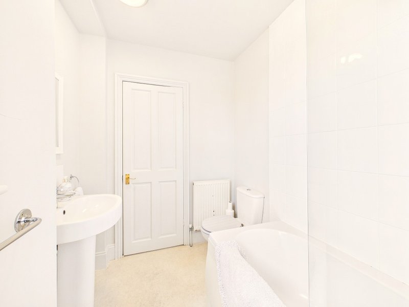 Clean white bathroom with pedestal sink, bathtub, toilet and wooden floor