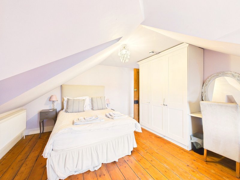 Bright attic bedroom with double bed, wooden floor, white wardrobe and sloped ceiling