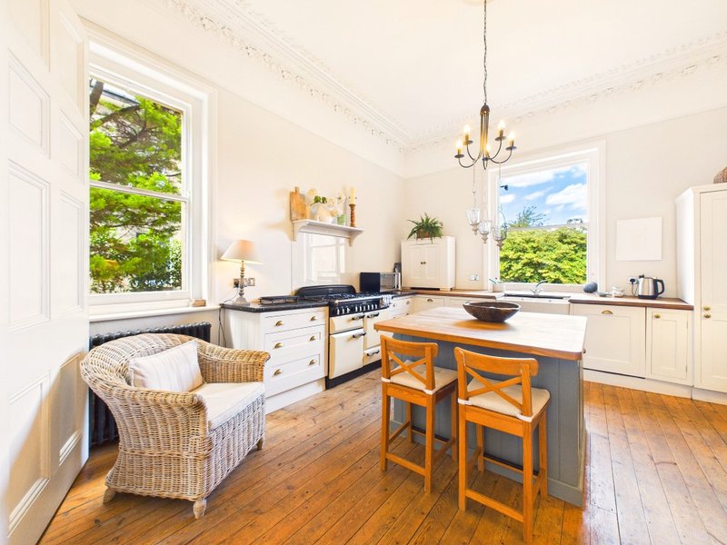 Bright kitchen with island, wooden bar stools, cream cabinetry, and large windows overlooking garden