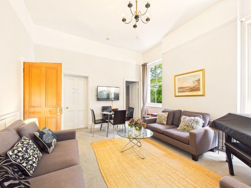 Spacious living room with grey sofas, wooden furniture, and bright natural light from windows