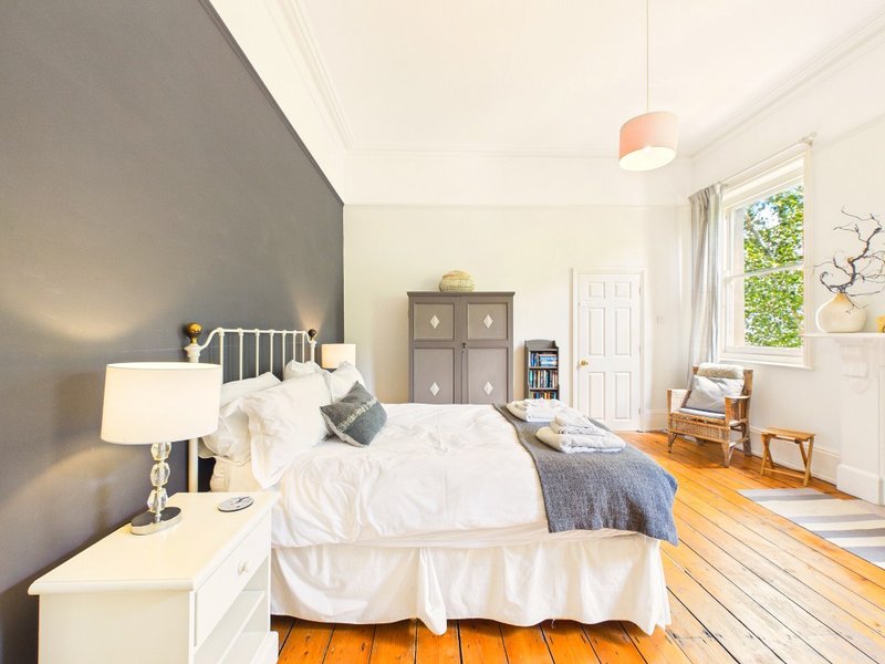 Bright bedroom with white metal bed frame, wooden floor, gray accent wall and natural light from windows