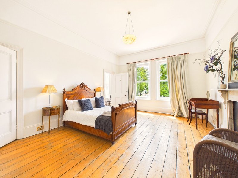 Bright bedroom with wooden bed, bedside lamps, wooden flooring, and French doors to garden