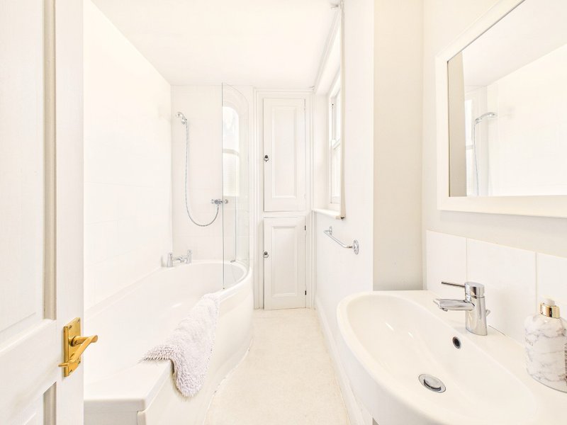 Modern bathroom with white tiles, walk-in shower, pedestal sink and gold fixtures