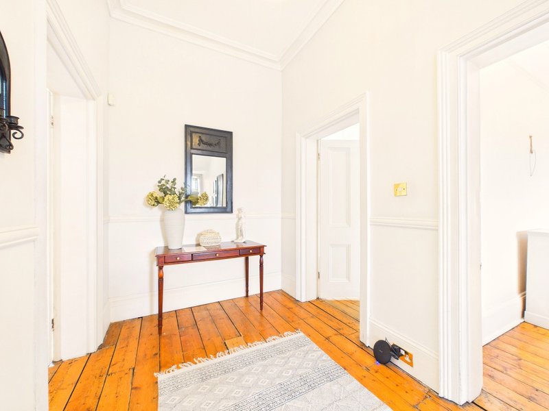 Bright hallway with wooden floor, red console table, mirror and white doors