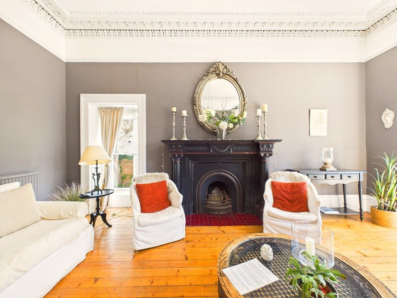 Spacious living room with fireplace, white sofas, orange accents, and wooden flooring