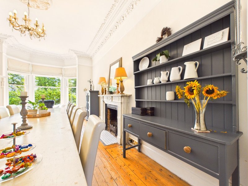 Bright dining room with fireplace, dark built-in shelving, sunflowers, and bay windows
