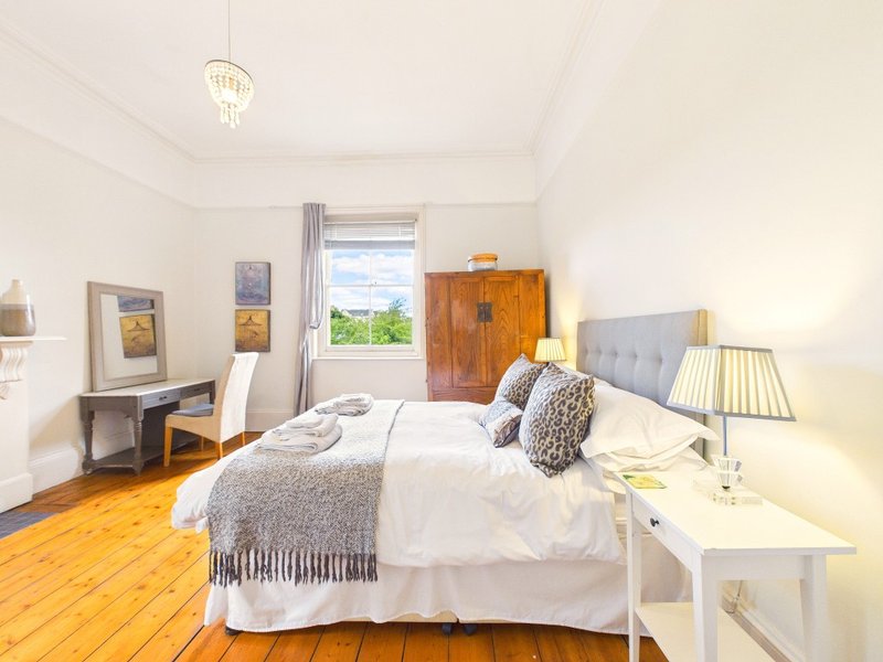 Bright bedroom with double bed, wooden floor, bedside tables, and garden view through door