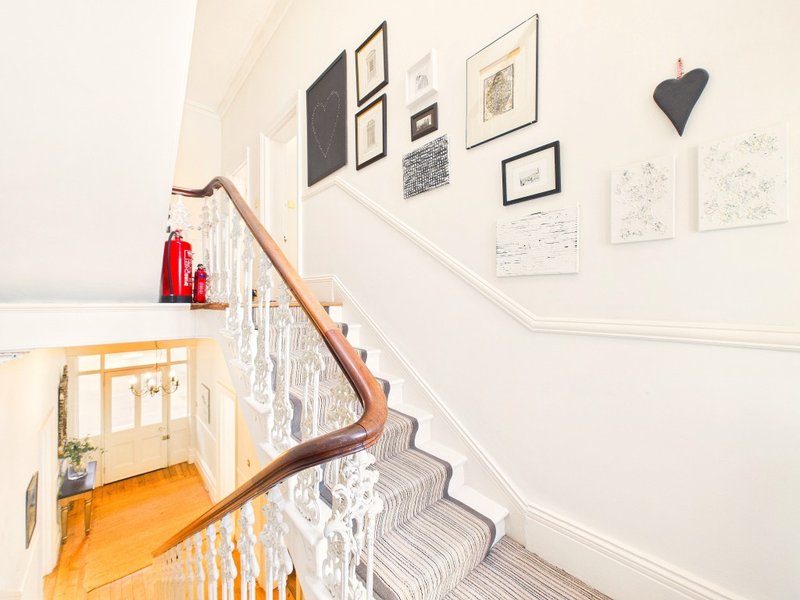 Staircase with wooden handrail, striped carpet, and framed wall art gallery