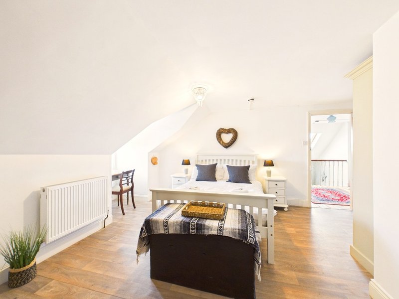 Bright loft bedroom with sloped ceiling, wooden floor, double bed and seating area