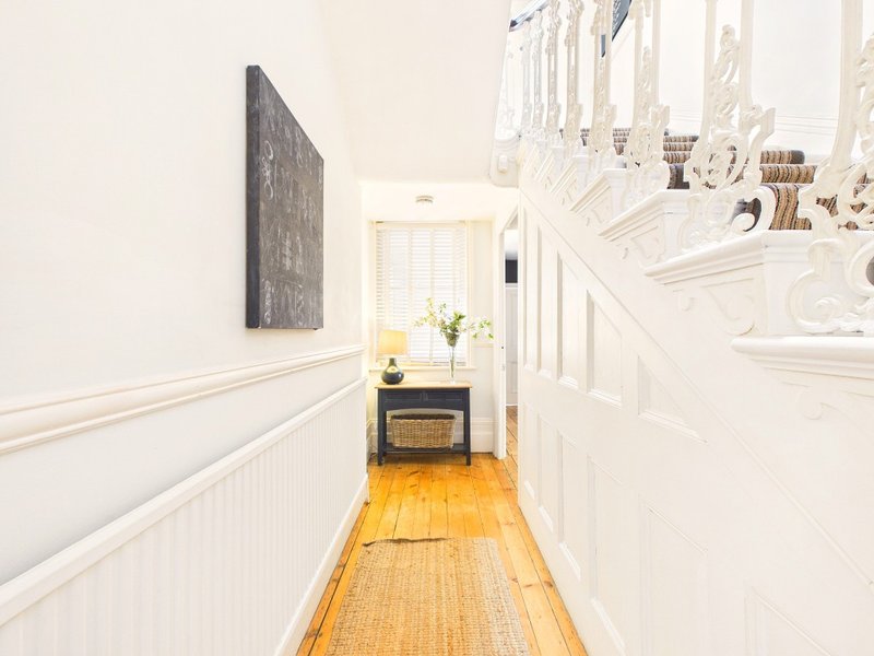 Narrow hallway with white wainscoting, wooden floor, staircase and wall-mounted chalkboard