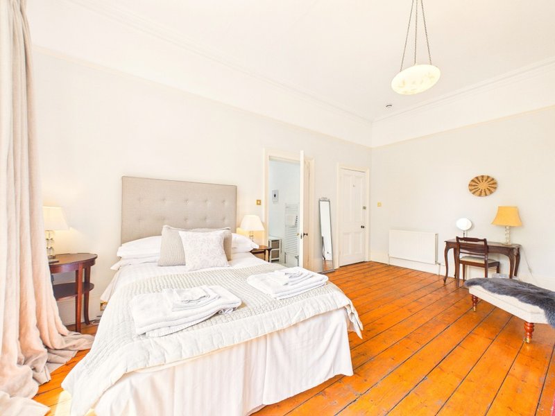 Bright bedroom with double bed, wooden floor, desk and bedside tables with lamps