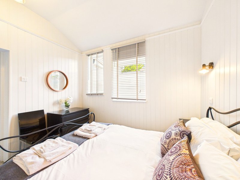 Bright bedroom with double bed, wooden desk, round mirror, and shuttered windows