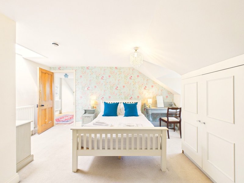 Bright attic bedroom with double bed, crib, floral wallpaper, and wooden door