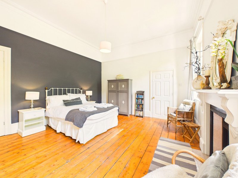 Spacious bedroom with double bed, wooden floor, fireplace and grey accent wall