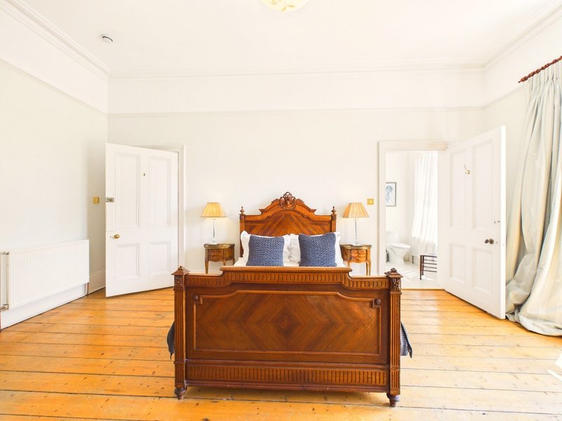 Spacious bedroom with wooden bed, two bedside lamps, wooden flooring and white doors
