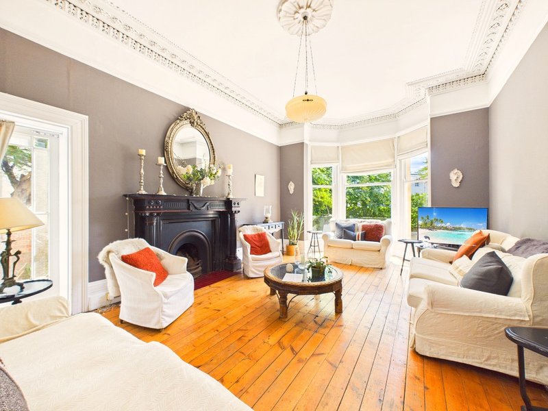 Bright living room with fireplace, cream armchairs, wooden floor and bay windows