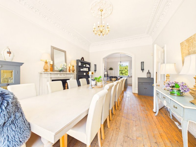 Bright dining room with white table, wooden chairs, chandelier and hardwood flooring