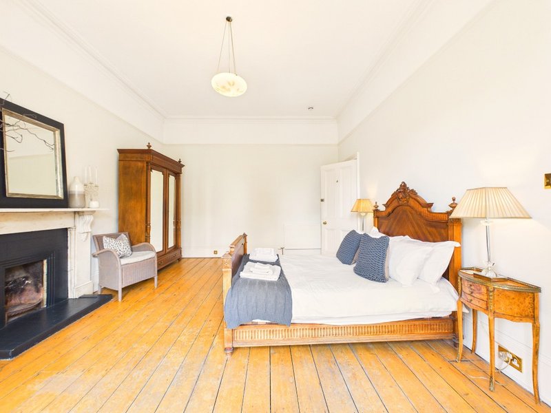 Spacious bedroom with wooden bed, fireplace, armchair, and hardwood flooring