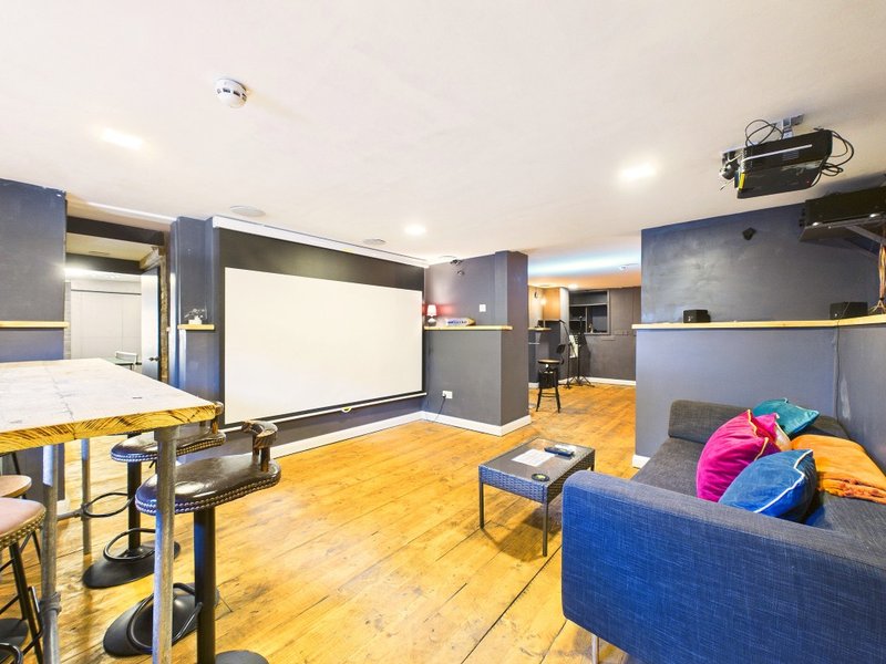 Open-plan recreation room with whiteboard, blue sofa, wooden flooring and bright ceiling lights