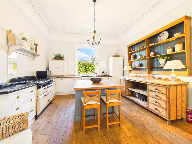 Bright kitchen with white range cooker, wooden island with orange stools, and yellow shelving units