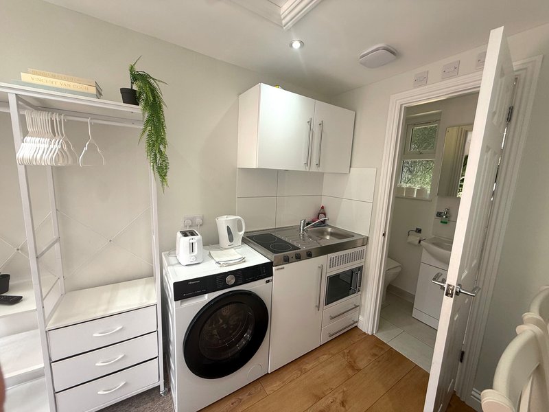 Modern kitchen with white cabinetry, washing machine, oven, and wooden flooring