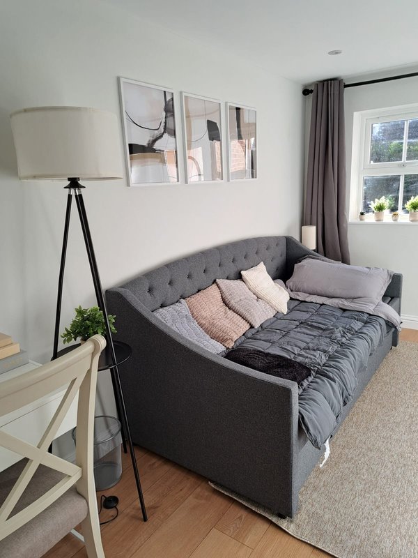 Bright bedroom with gray upholstered daybed, floor lamp, wall art, and window with curtains