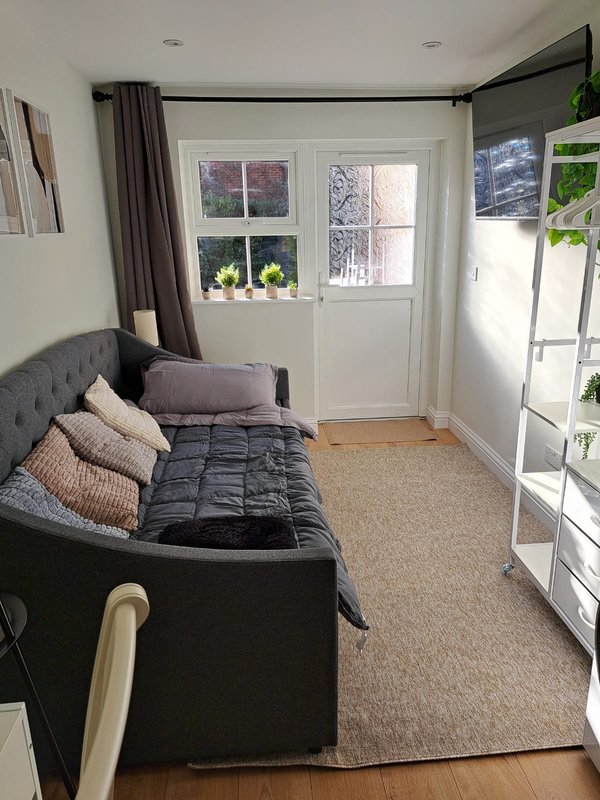 Bedroom with dark upholstered bed, striped cushions, curtains, and door to garden area